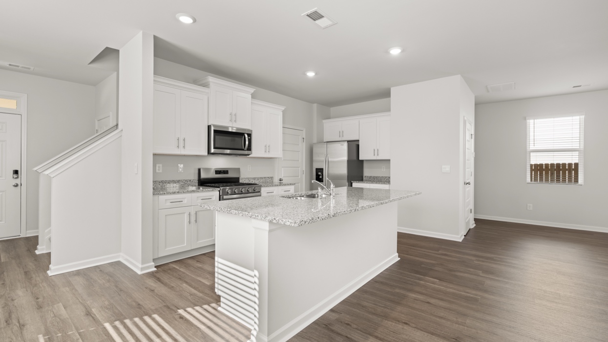 Bright modern kitchen with granite counters, stainless steel appliances, and large center island opening to living and dining space.