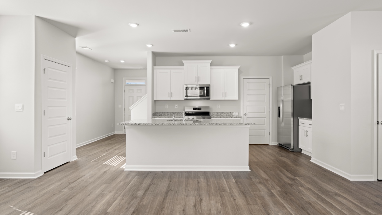 Bright modern kitchen with granite counters, stainless steel appliances, and large center island opening to living and dining space.
