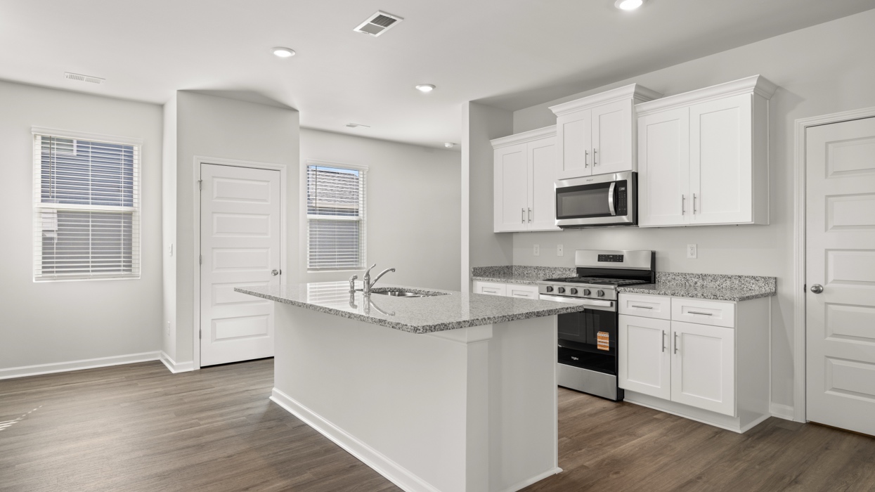 Bright modern kitchen with granite counters, stainless steel appliances, and large center island opening to living and dining space.