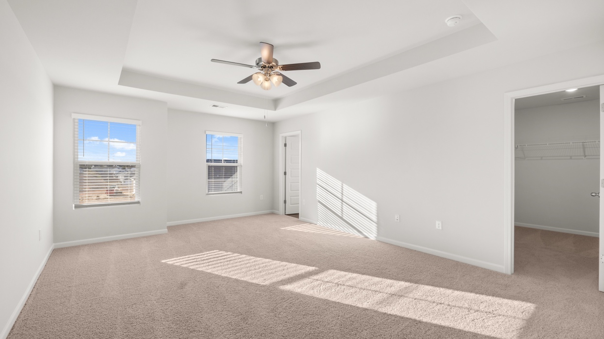 Primary bedroom with tray ceilings, ceiling fan, large closet, and en suite bath