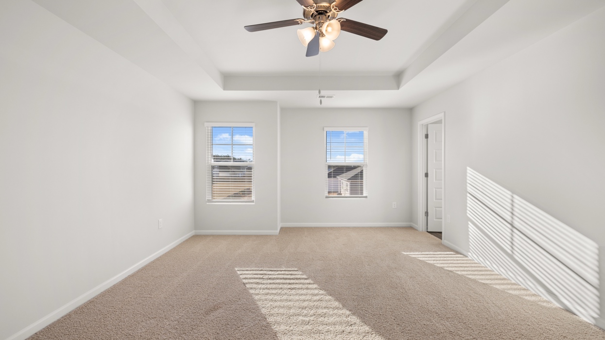 Primary bedroom with tray ceilings, ceiling fan, large closet, and en suite bath