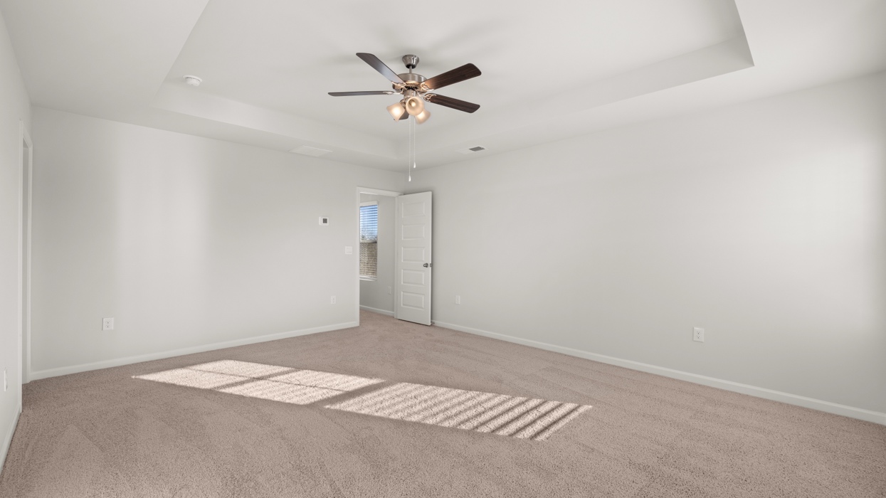Primary bedroom with tray ceilings, ceiling fan, large closet, and en suite bath