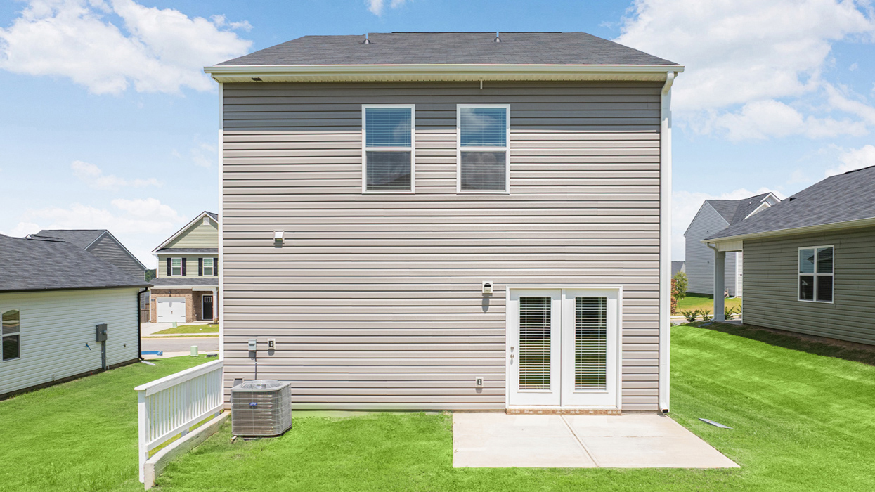 Rear of two story greige home with back patio and lush lawn