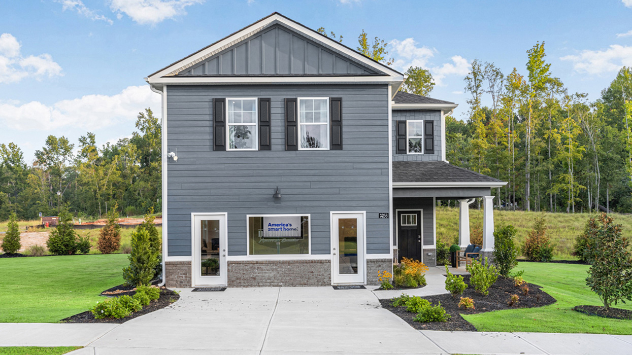Two story blue home with lush landscaping in a wooded setting