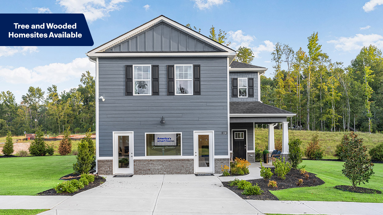 Two story blue home with lush landscaping in a wooded setting