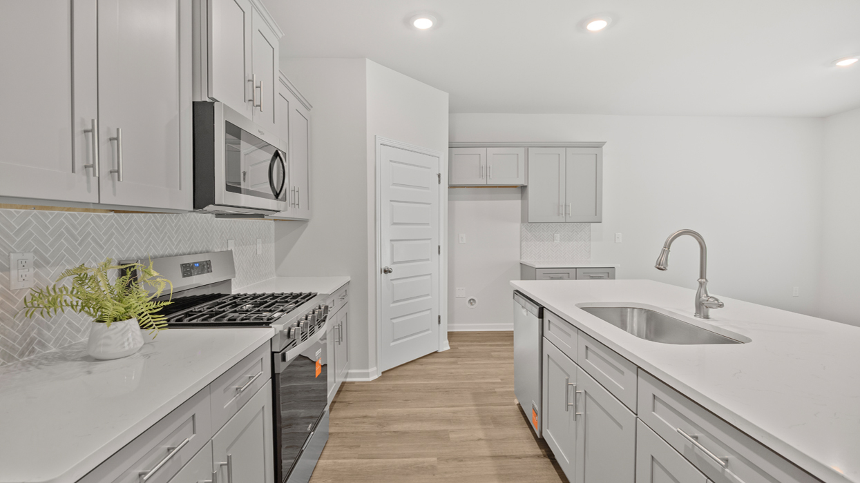Kitchen with gray shaker cabinets, chevron tile backsplash, quartz countertops, and large center island with bar seating
