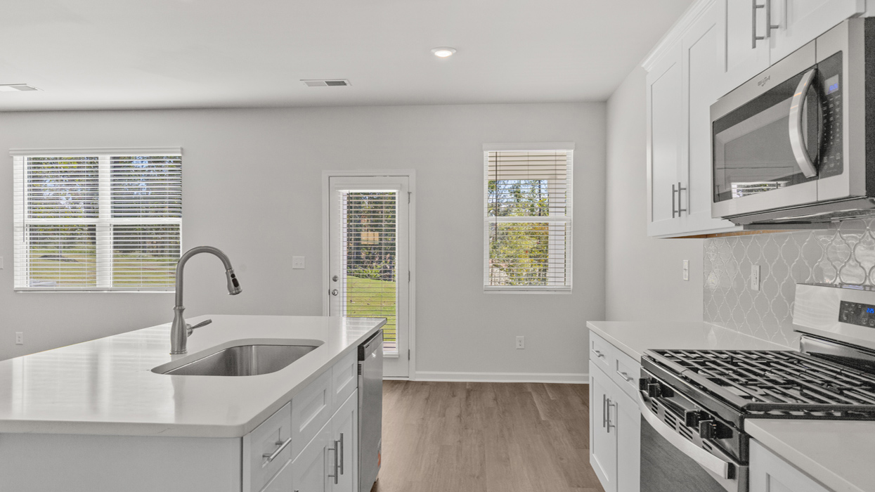 Modern kitchen with quartz countertops, shaker cabinets, tile backsplash, and stainless gas appliances with large center island