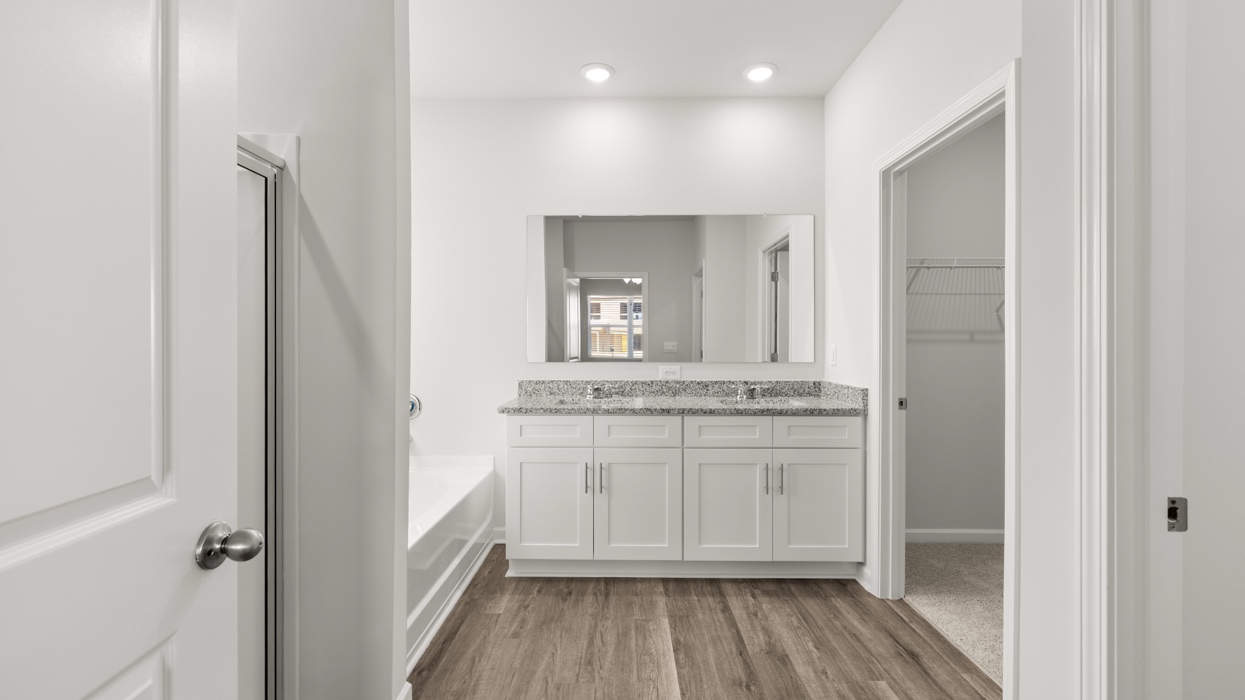 Primary bath on main level with double vanity, garden tub, shower with glass door, and large closet