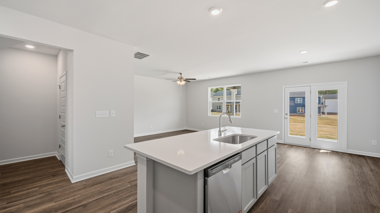 Open plan featuring kitchen with quartz countertops, tile backsplash, corner pantry, stainless appliances, and large center island overlooking dining and living room.