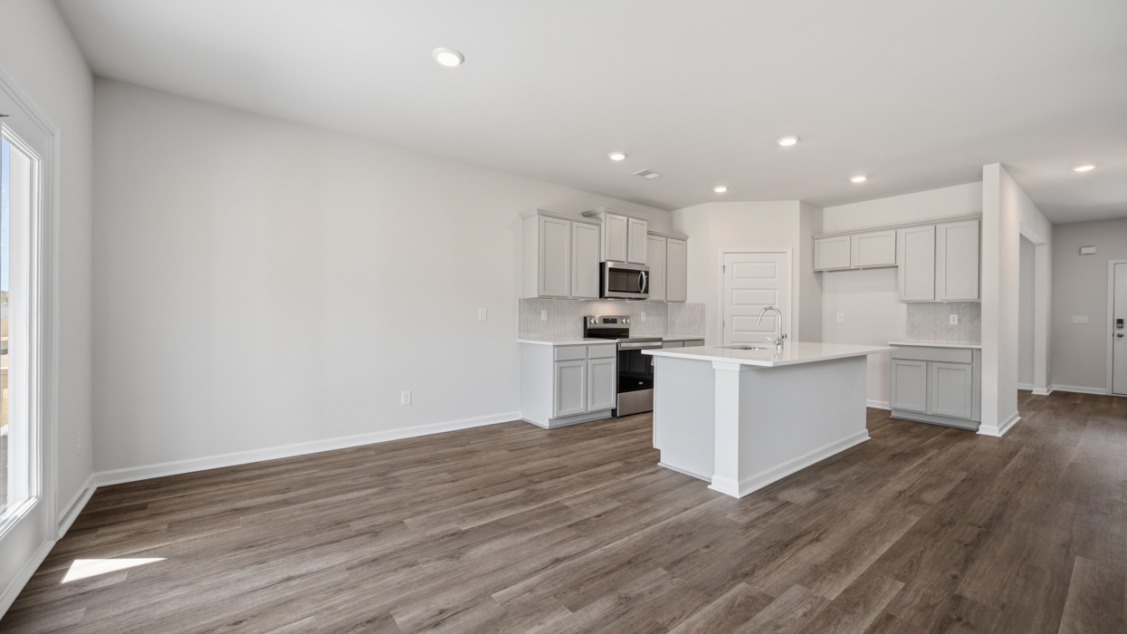 Open plan featuring kitchen with quartz countertops, tile backsplash, corner pantry, stainless appliances, and large center island overlooking dining and living room.