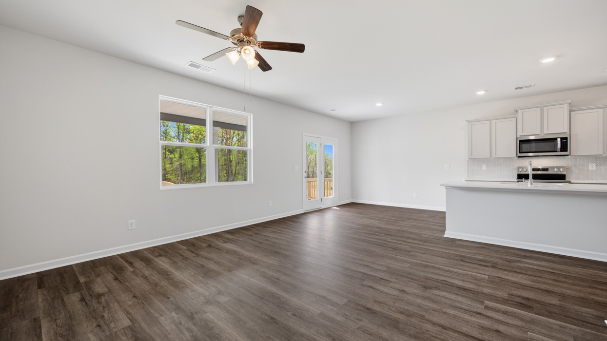 Open plan featuring kitchen with quartz countertops, tile backsplash, corner pantry, stainless appliances, and large center island overlooking dining and living room.