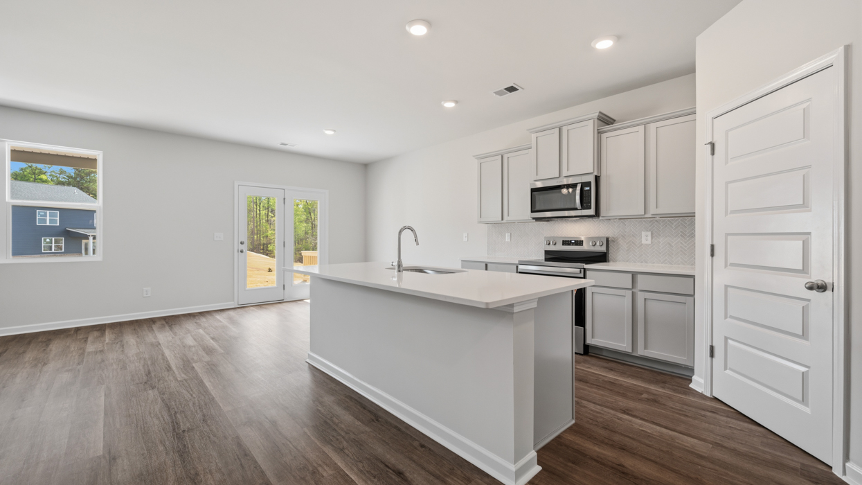 Bright modern kitchen with shaker cabinets, quartz countertops, tile backsplash, pantry, and stainless appliances.