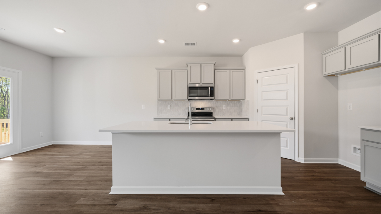 Bright modern kitchen with shaker cabinets, quartz countertops, tile backsplash, pantry, and stainless appliances.