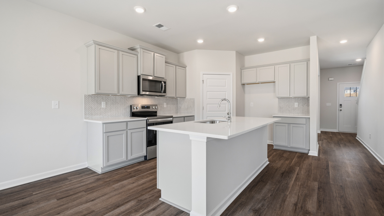Bright modern kitchen with shaker cabinets, quartz countertops, tile backsplash, pantry, and stainless appliances.