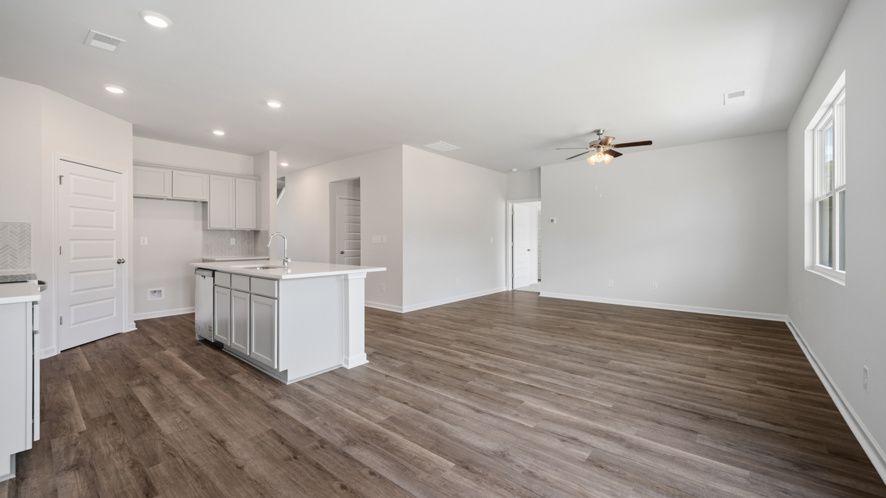 Bright modern kitchen with shaker cabinets, quartz countertops, tile backsplash, pantry, and stainless appliances open to main living area.