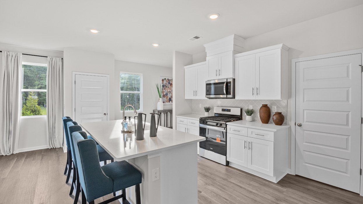 Modern kitchen with shaker cabinets, quartz countertops, stainless appliances, tile backsplash, pantry, and center island overlooking open living and dining area.
