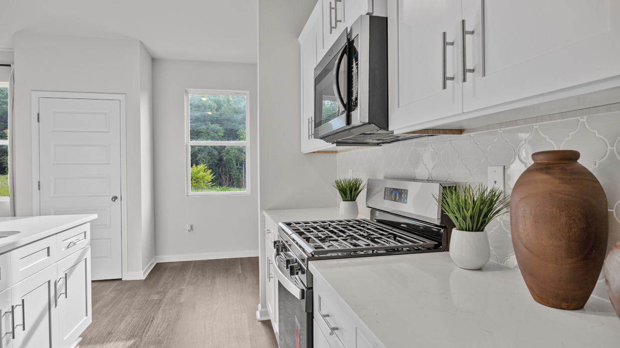 Modern kitchen with shaker cabinets, quartz countertops, stainless appliances, tile backsplash, pantry, and center island overlooking open living and dining area.