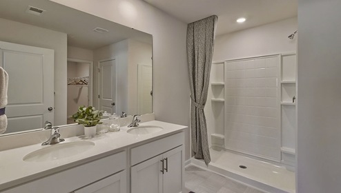 Primary bathroom with double sinks, standing shower, and white cabinets and counters