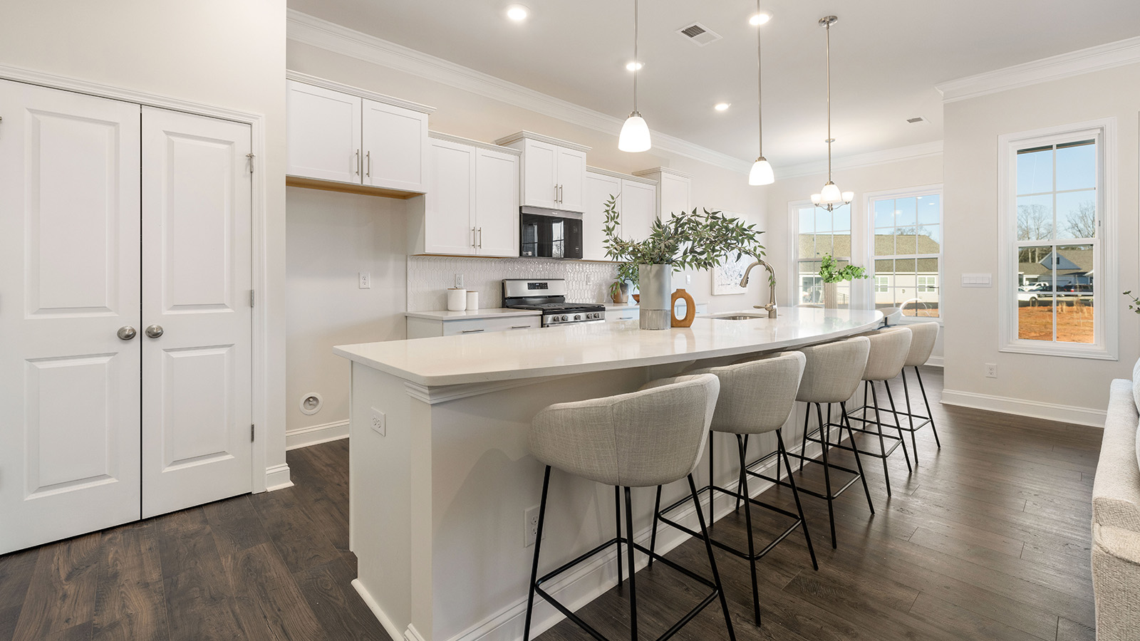 Kitchen and island with wood floors, white cabinets and counters, stainless steel appliances, and seating at island bar