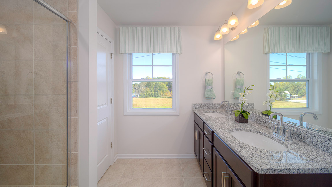 Primary bathroom with double sinks, brown cabinets, and glass door shower