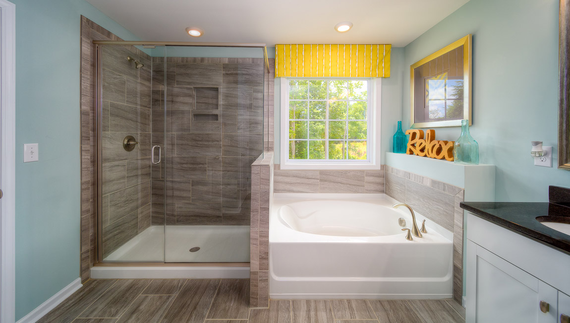 Primary bathroom with white cabinets, bathtub, and glass door shower