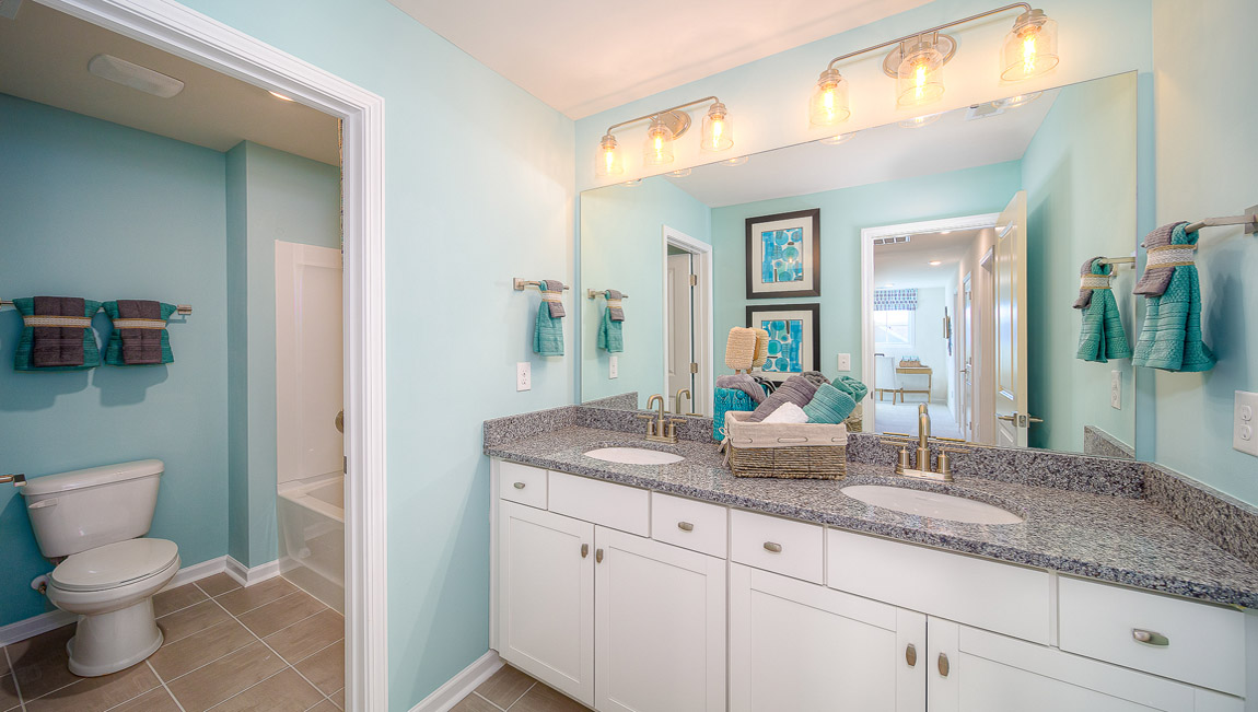 Bathroom with double sinks, white cabinets, and separate door to bathtub and toilet