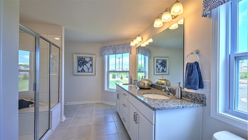 Bathroom with double sinks, glass door shower, white cabinets and large window