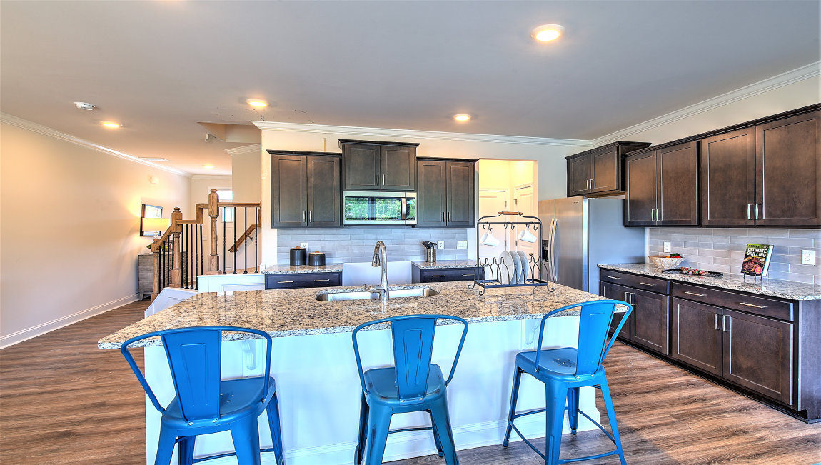 Open kitchen with island, wood floors, brown cabinets, living room in view
