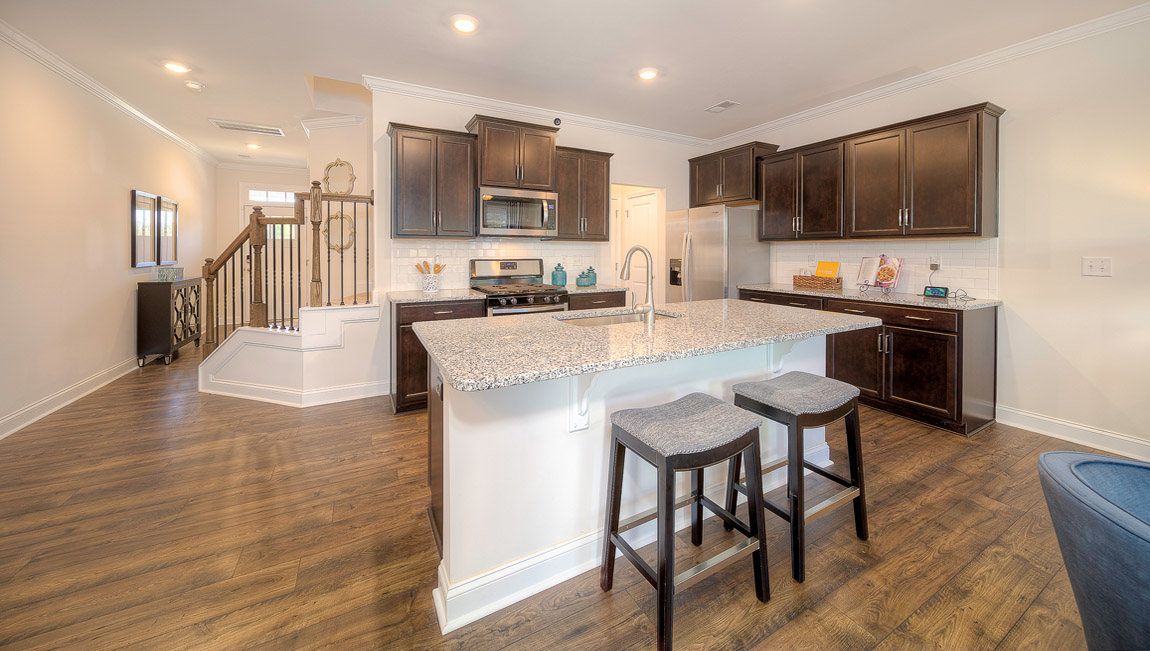 Open kitchen with island, wood floors, brown cabinets, living room in view