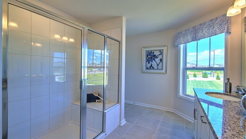 Bathroom with double sinks, glass door shower, white cabinets and large window