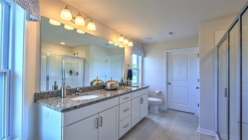 Bathroom with double sinks, glass door shower, white cabinets and large window