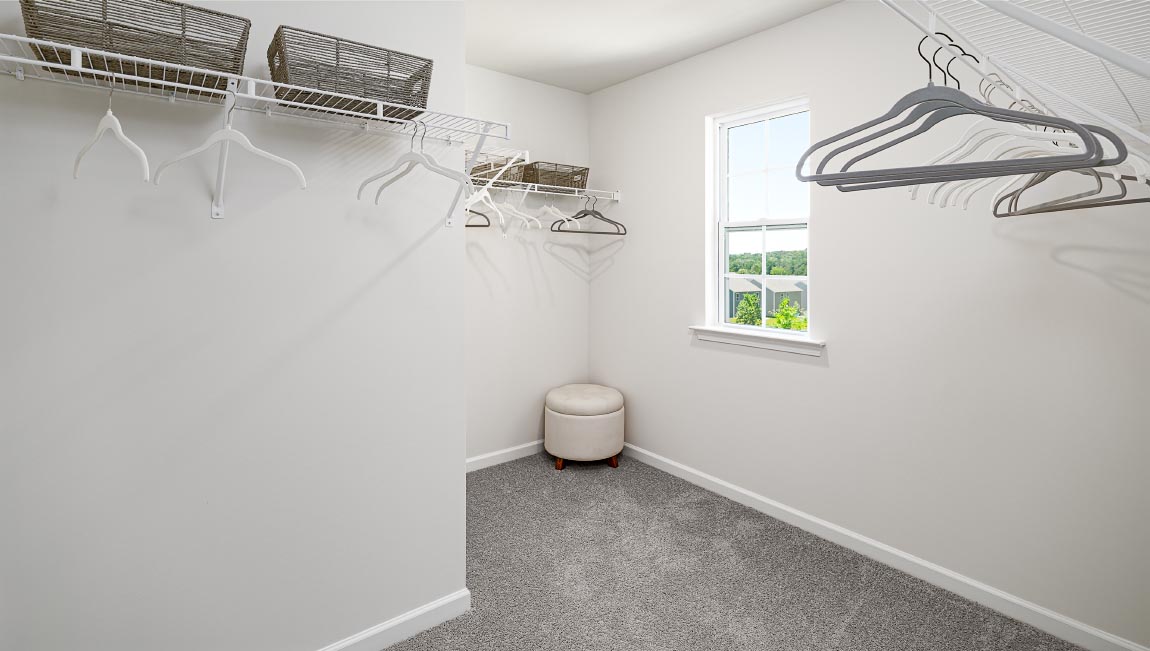 Primary walk in closet with carpet and small window. New Home in Asheville, North Carolina