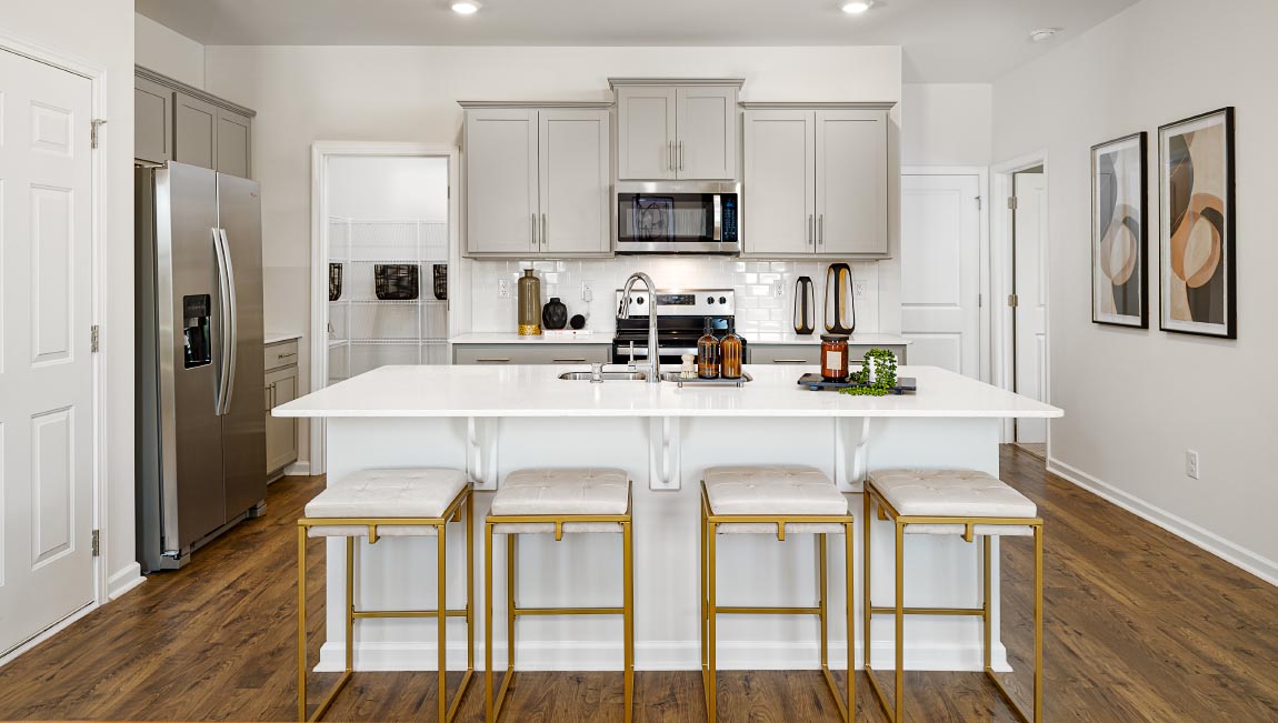 Kitchen and island with grey cabinets, white countertops, white subway tile backsplash, breakfast bar area and stainless steel appliances. New Home in Asheville, North Carolina