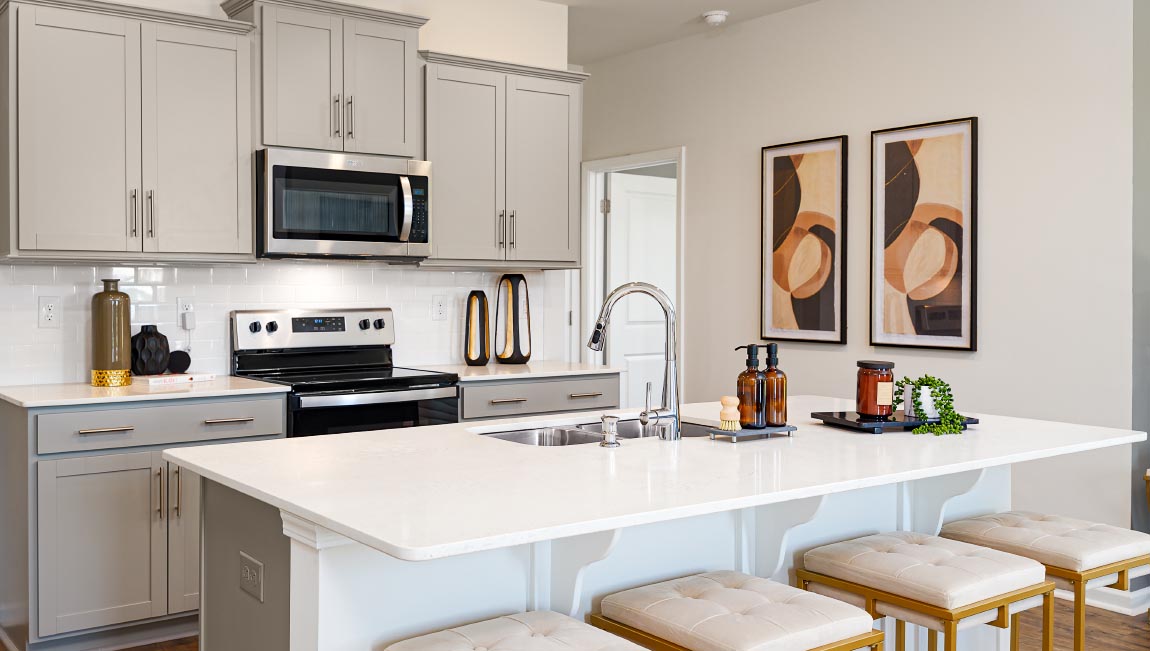 Kitchen and island with grey cabinets, white countertops, white subway tile backsplash, breakfast bar area and stainless steel appliances. New Home in Asheville, North Carolina
