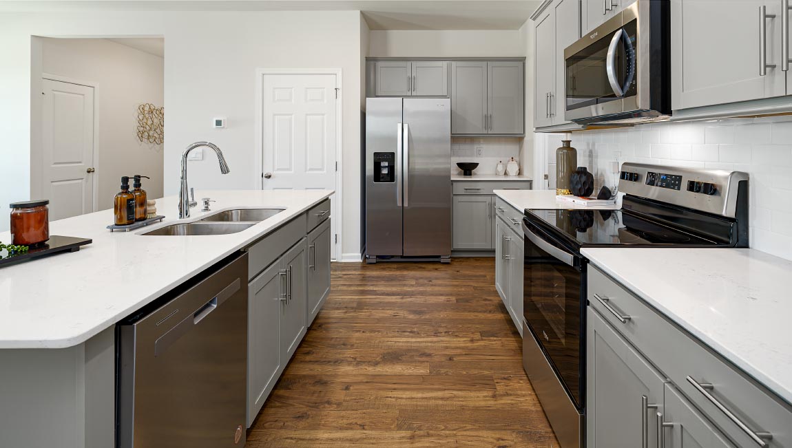 Kitchen and island with grey cabinets, white countertops, white subway tile backsplash, breakfast bar area and stainless steel appliances. New Home in Asheville, North Carolina