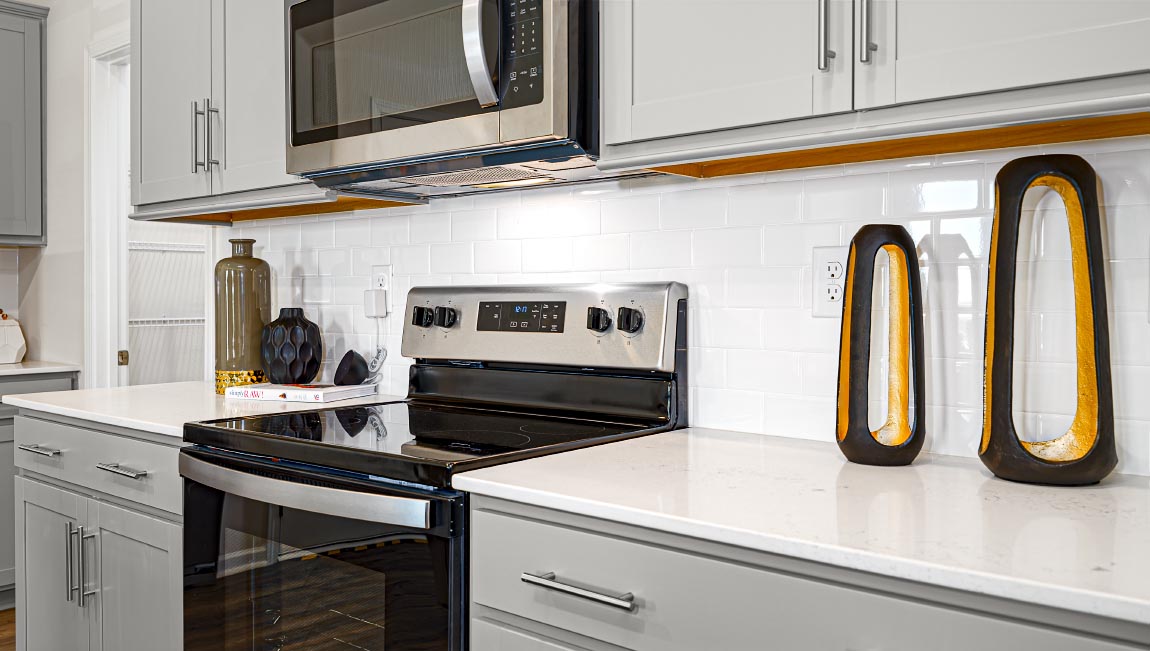 Kitchen and island with grey cabinets, white countertops, white subway tile backsplash, breakfast bar area and stainless steel appliances. New Home in Asheville, North Carolina