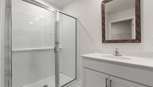 Bathroom with double sinks, white cabinets and counters, with glass door shower