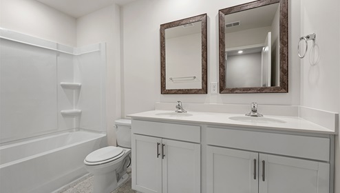 Bathroom with double sinks, white cabinets, counters and bathtub
