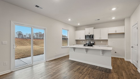 Kitchen and island with white cabinets and countertops, and stainless steel appliances. View of back sliding glass door