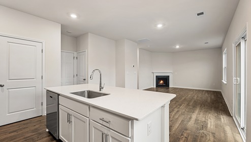 Kitchen and island with white cabinets and countertops, and stainless steel appliances View of living room with fireplace