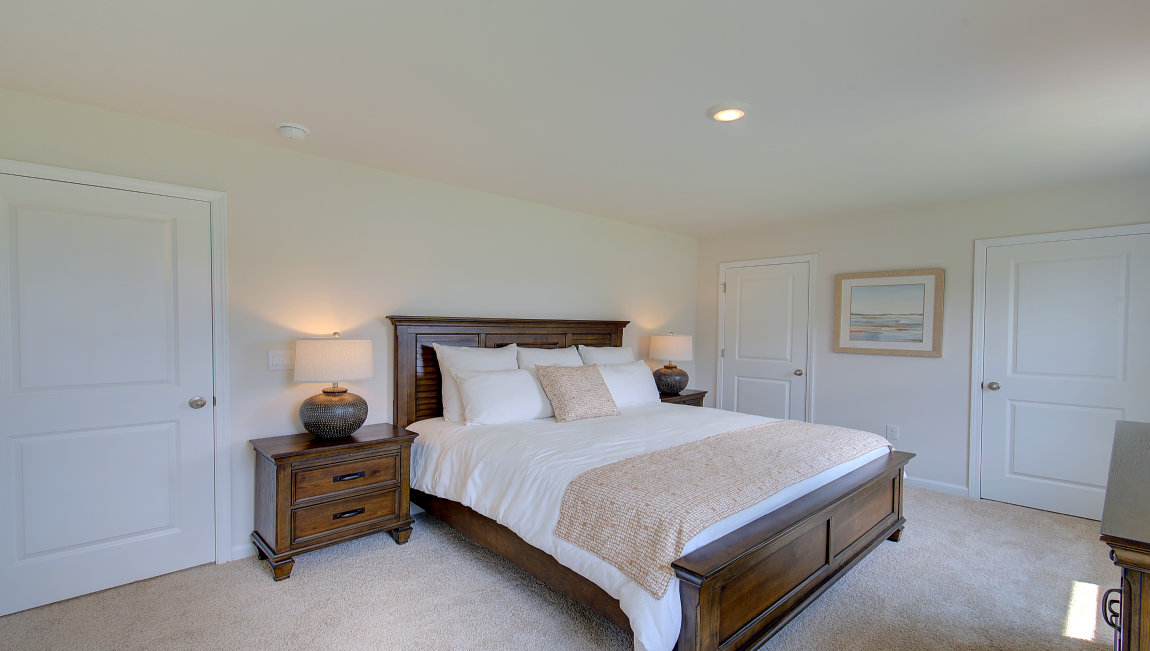 Primary bedroom with beige carpet and two windows. New Homes in Asheville, North Carolina