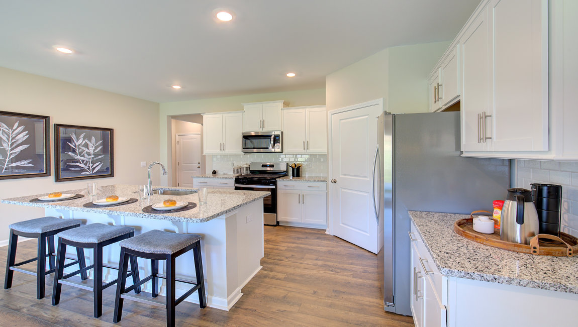 Kitchen and island with white cabinets and subway tiles and stainless steel appliances