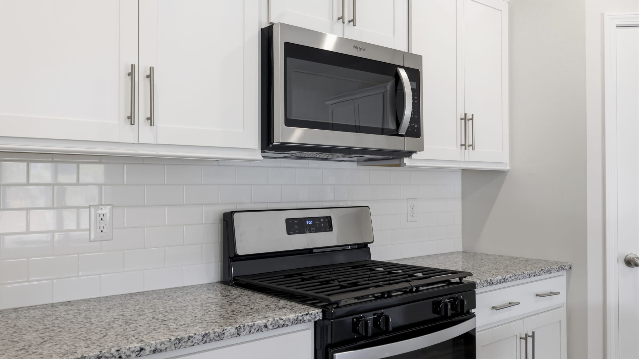 Close up view of kitchen with white cabinets and gas appliances