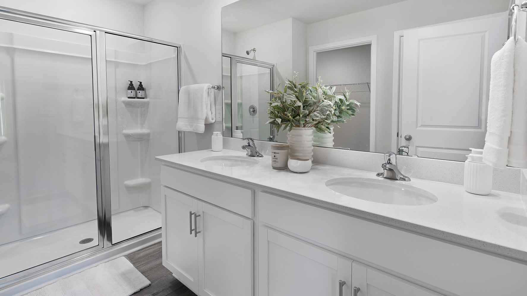 Bathroom with double sinks, white counters, cabinets and glass door shower