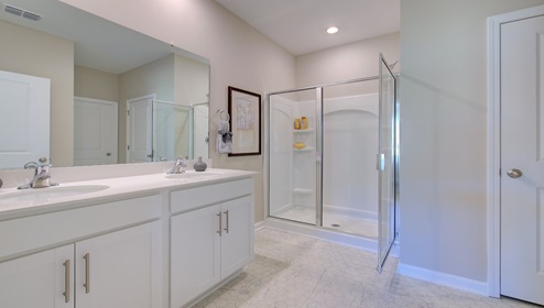 Primary bathroom with double sink vanity, white cabinets, and standing glass door shower