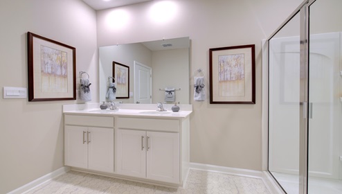 Primary bathroom with double sink vanity, white cabinets, and standing glass door shower