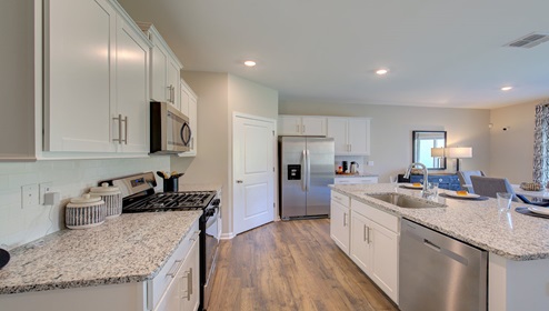 Kitchen and island wit white cabinets, granite counters, white subway tile backsplash, and stainless steel appliances