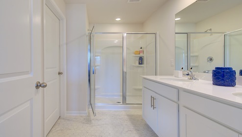 Primary bathroom with double sink vanity, white counters and cabinets, and standing glass door shower