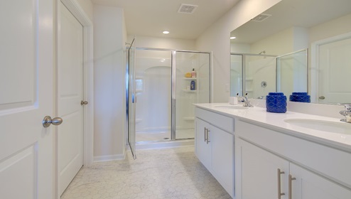 Primary bathroom with double sink vanity, white counters and cabinets, and standing glass door shower
