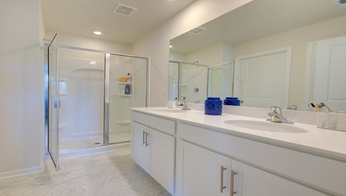 Primary bathroom with double sink vanity, white counters and cabinets, and standing glass door shower